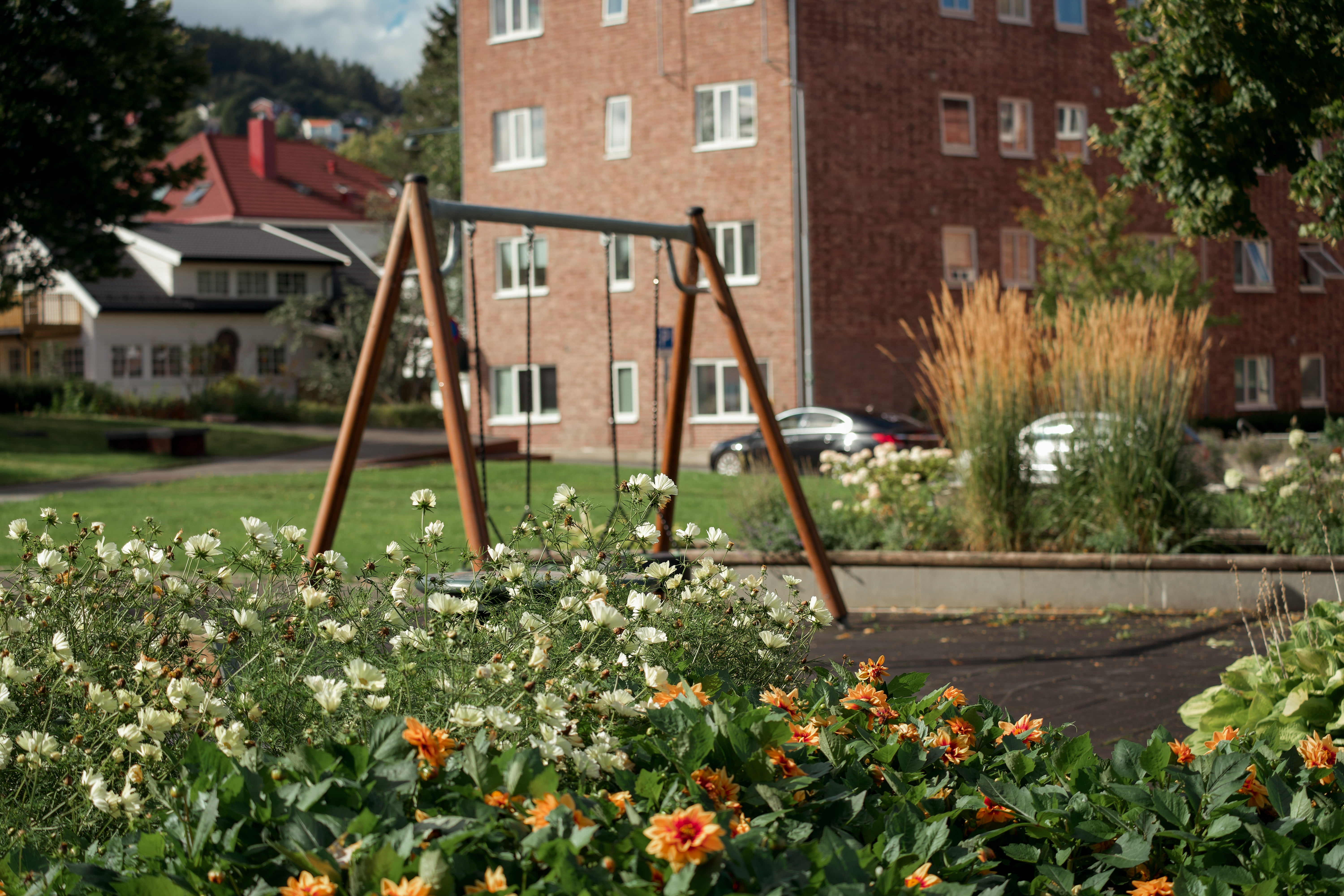 Blomebed og husker i ein grøn felles hage framfor ei raud murbygning i eit borettslag.