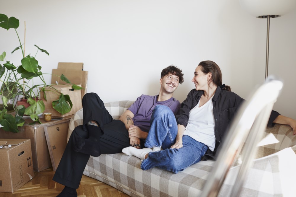 Ein mann og ei kvinne sit på sofaen omgitt av flyttekassar.