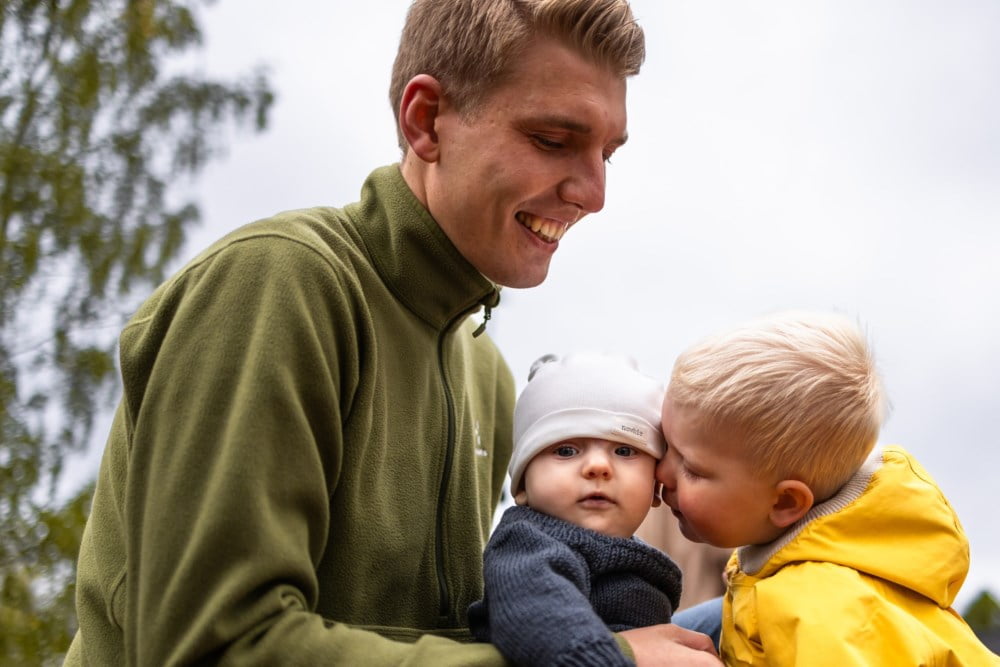 Ein mann held ein baby som får eit nuss på kinnet av ein liten gut