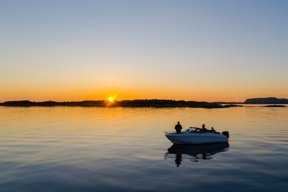 Ein båt på stille vatn under ein vakker solnedgang, med øyar i horisonten.