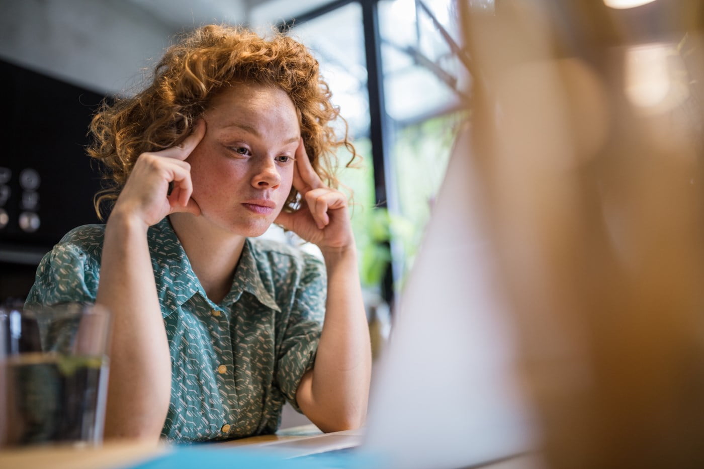 Ein kvinne med raudt hår ser tankefullt på dataskjermen sin, truleg i ferd med å utforske dei nye digitale løysingane for betalingsformat. Heldigvis er ho kunde i ein bank som er beredt til å tilby rettleiing og støtte om det dukkar opp spørsmål. Biletet fangar ein uformell atmosfære og speglar banken sitt engasjement for enkel og tilgjengeleg kundeteneste under overgangen til ISO 20022 XML-formatet.